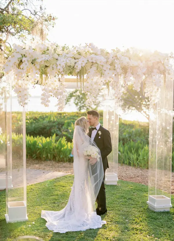 a-large-acrylic-wedding-arbor-covered-with-lush-white-orchids-and-with-a-view-of-a-field-as-a-backdrop a-large-acrylic-wedding-arbor-covered-with-lush-white-orchids-and-with-a-view-of-a-field-as-a-backdrop
